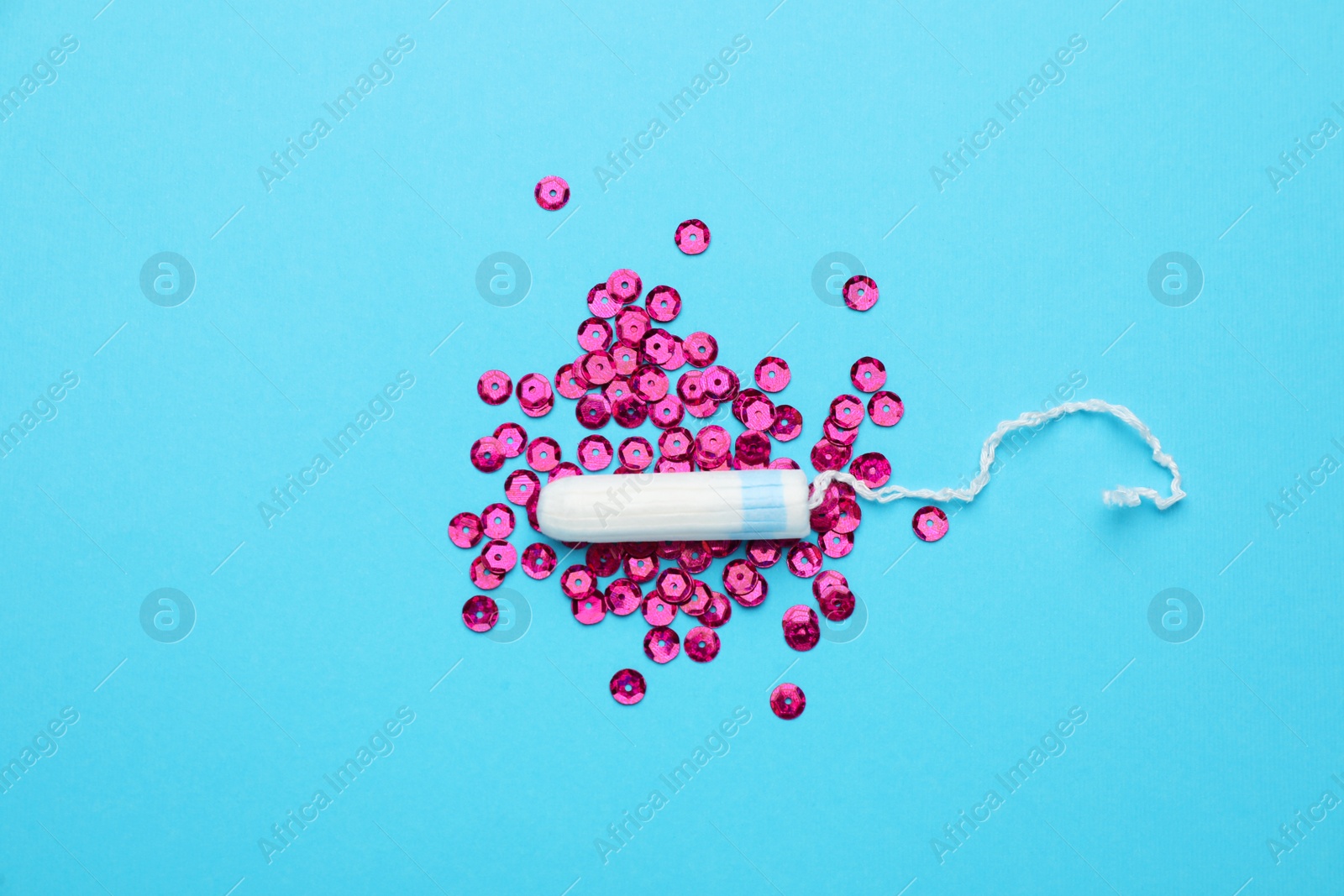 Photo of Tampon and pink sequins on light blue background, flat lay. Menstrual hygiene product