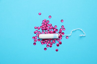Tampon and pink sequins on light blue background, flat lay. Menstrual hygiene product