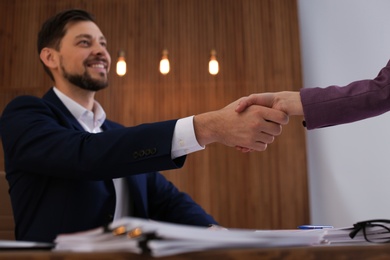 Photo of Office employees shaking hands over table with documents at workplace