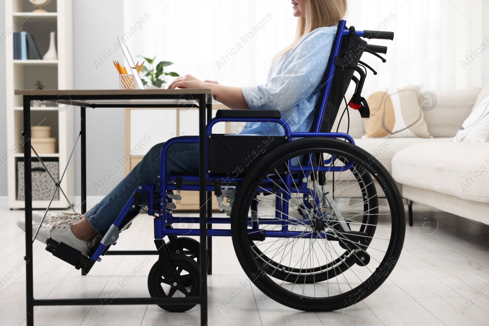 Photo of Woman in wheelchair using laptop at table in home office, closeup