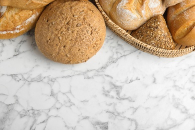 Loaves of different breads on white marble background, flat lay. Space for text