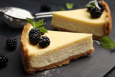 Photo of Pieces of delicious cheesecake with blackberries on slate plate, closeup