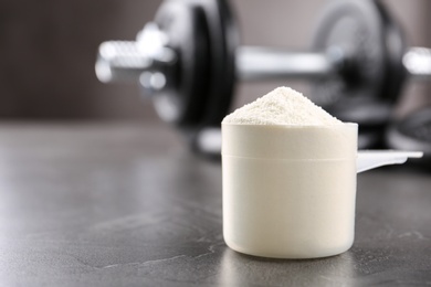 Photo of Measuring scoop of protein powder on grey table. Space for text