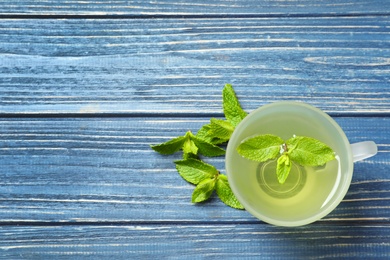 Photo of Cup with hot aromatic mint tea and fresh leaves on wooden table, top view