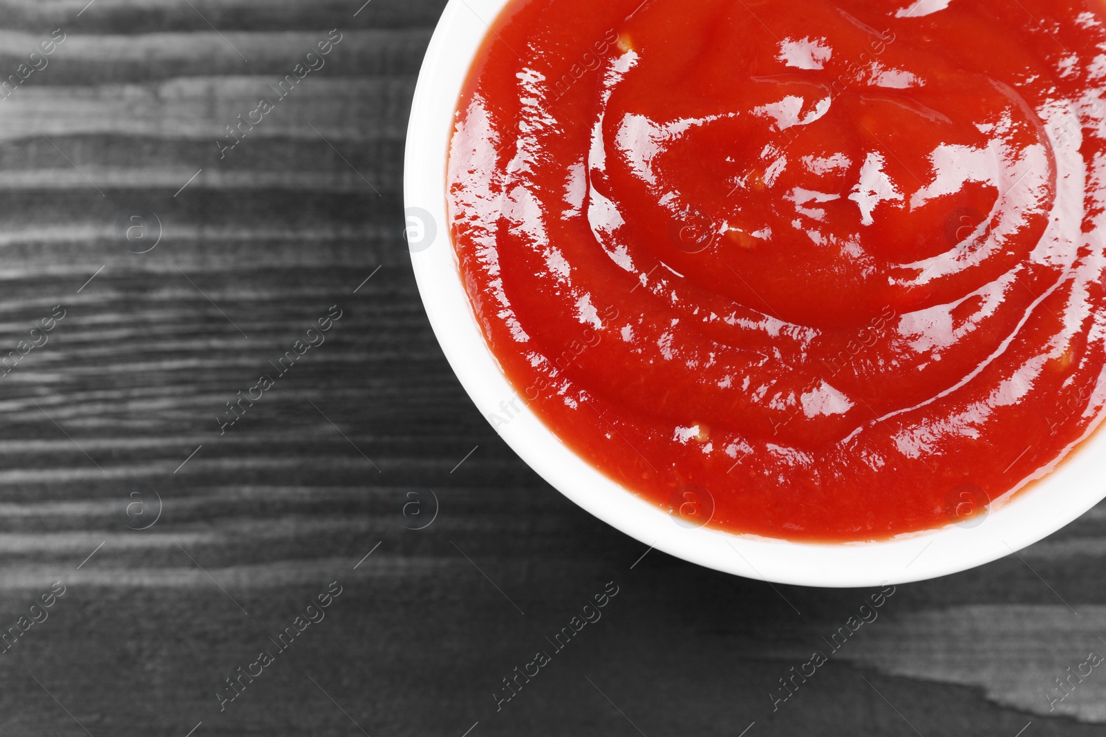 Photo of Delicious ketchup in bowl on black wooden table, top view with space for text. Tomato sauce