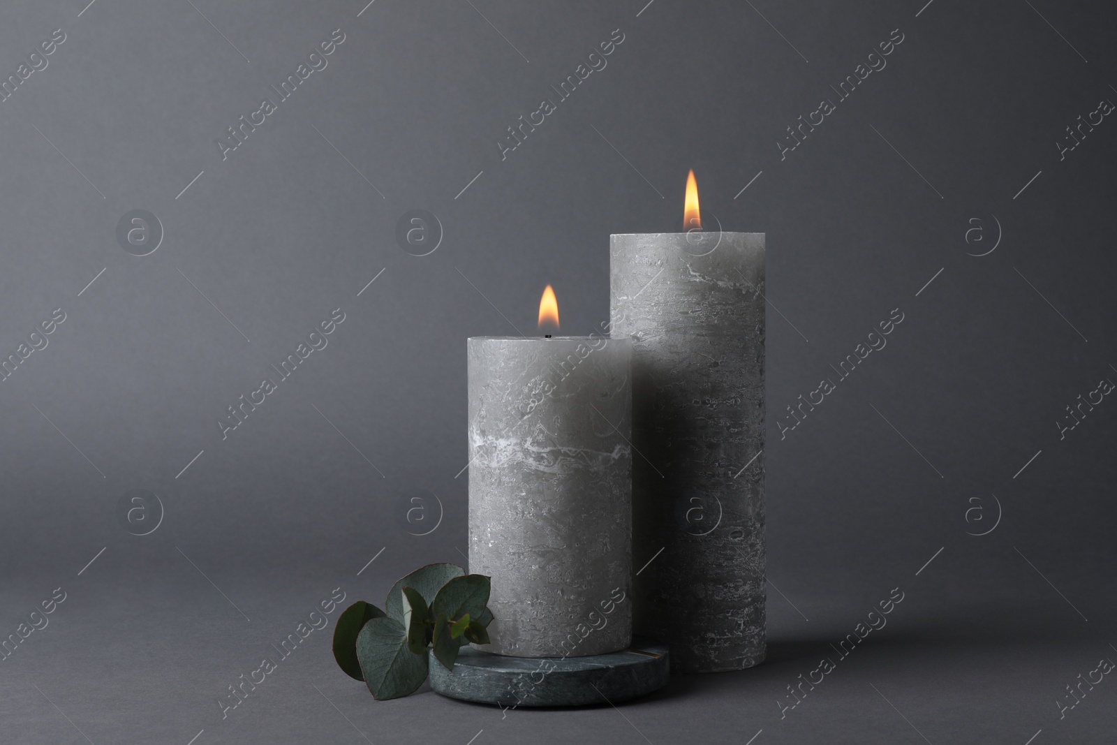 Photo of Burning candles with green branch on grey background