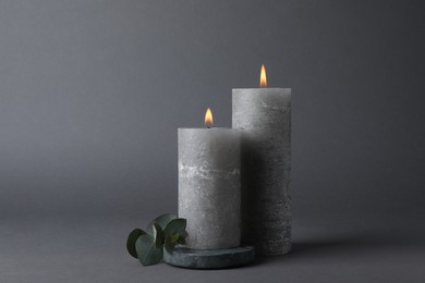 Burning candles with green branch on grey background