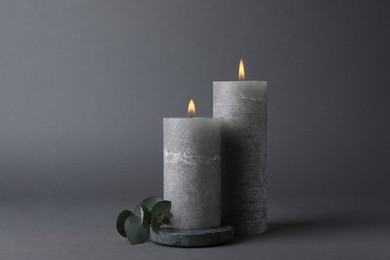 Photo of Burning candles with green branch on grey background