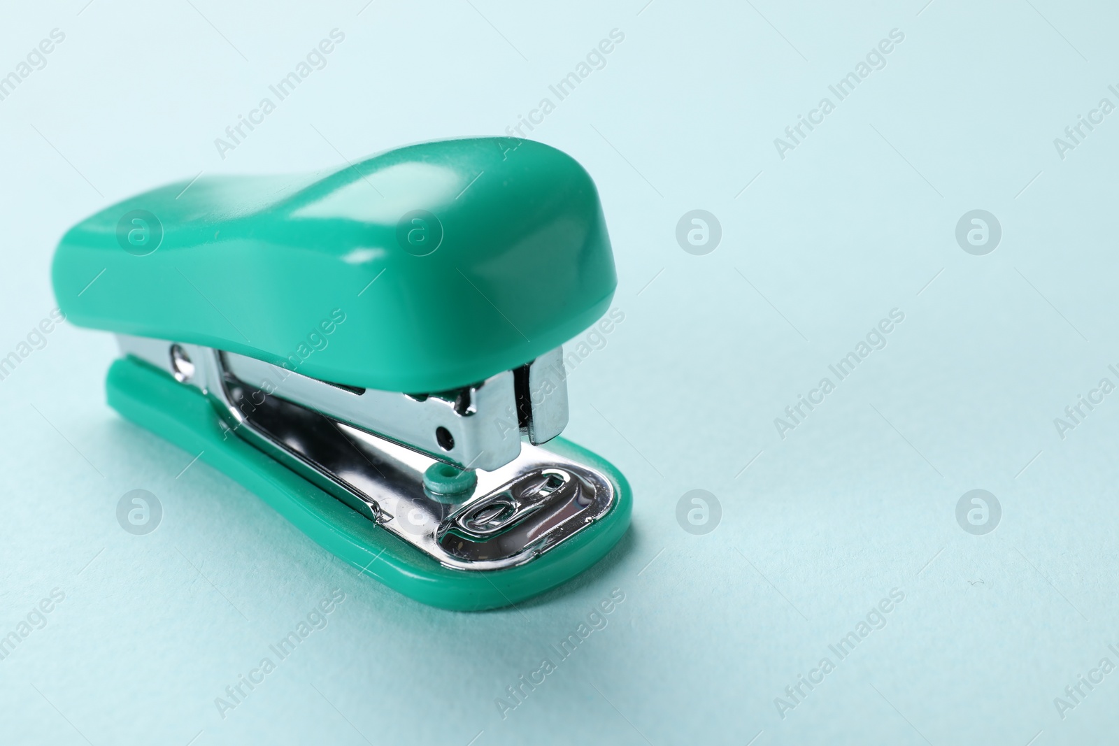 Photo of Turquoise stapler on light blue background, closeup. Space for text