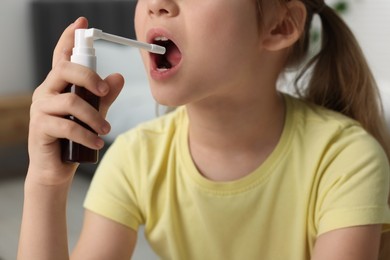 Little girl using throat spray at home, closeup