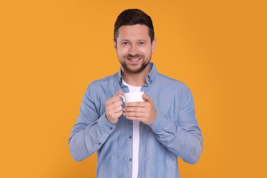 Portrait of happy man holding white mug on orange background