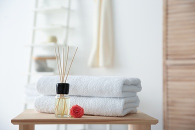 Photo of Reed air freshener and stack of towels on table against blurred background