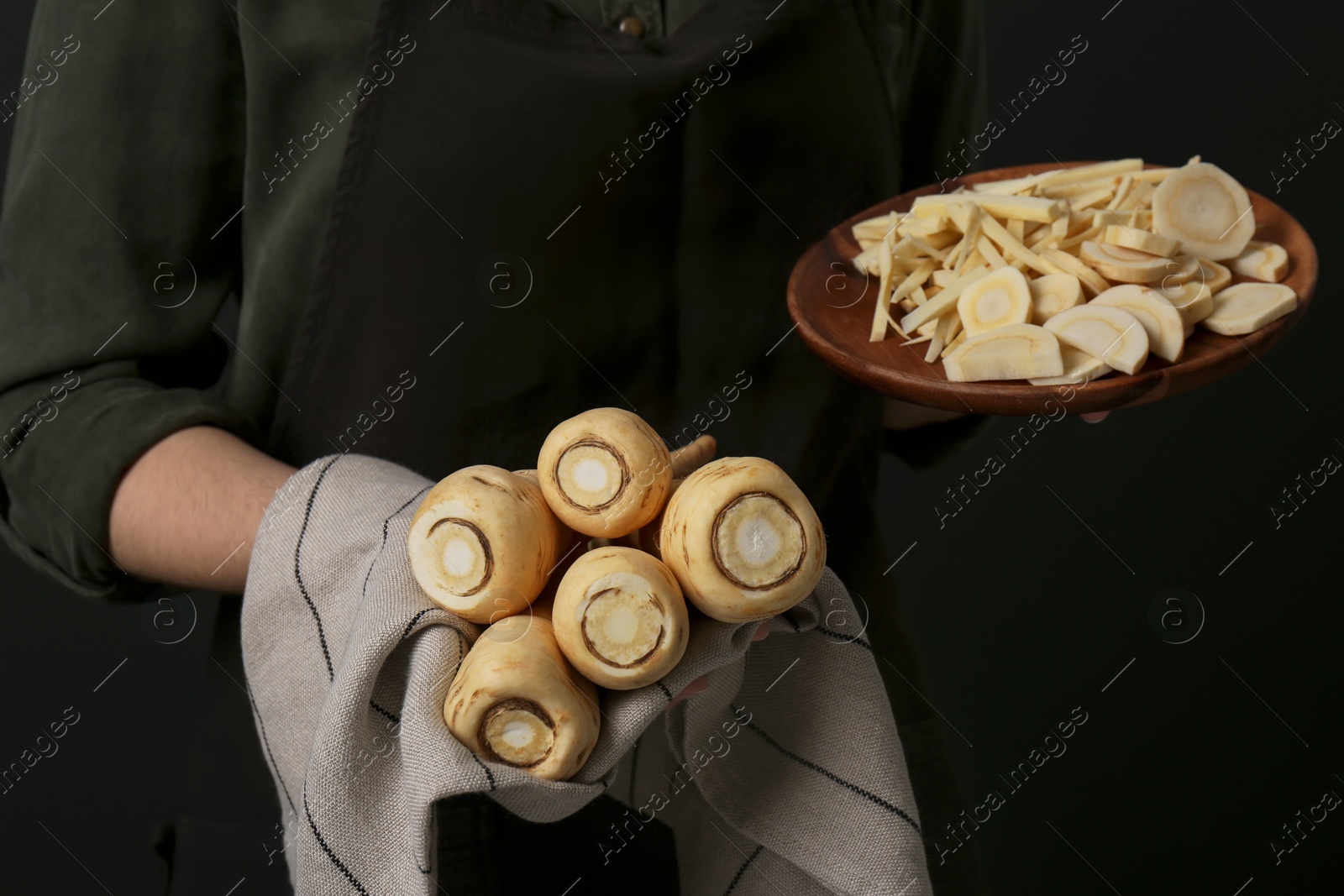 Photo of Woman holding whole and cut parsnips on black background, closeup