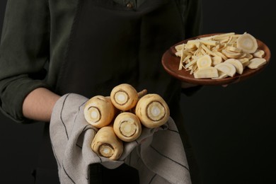 Woman holding whole and cut parsnips on black background, closeup