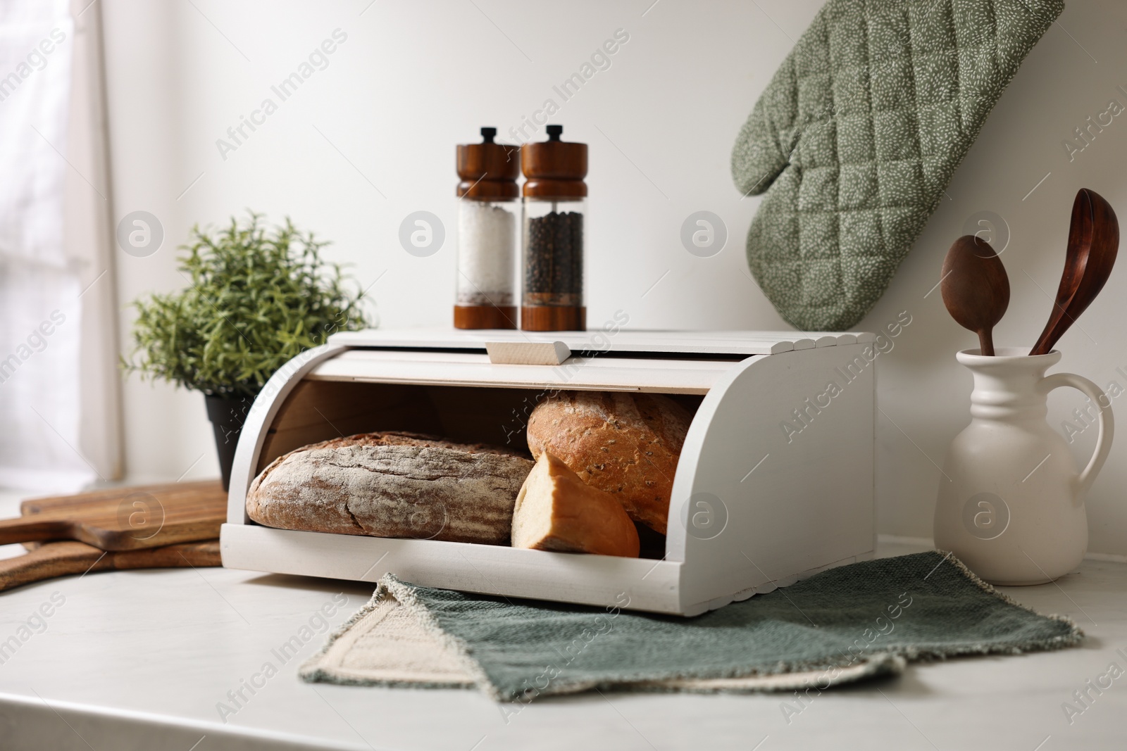 Photo of Wooden bread basket with freshly baked loaves on white marble table in kitchen