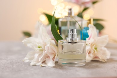 Bottles of perfume and beautiful lily flowers on table against beige background with blurred lights, closeup