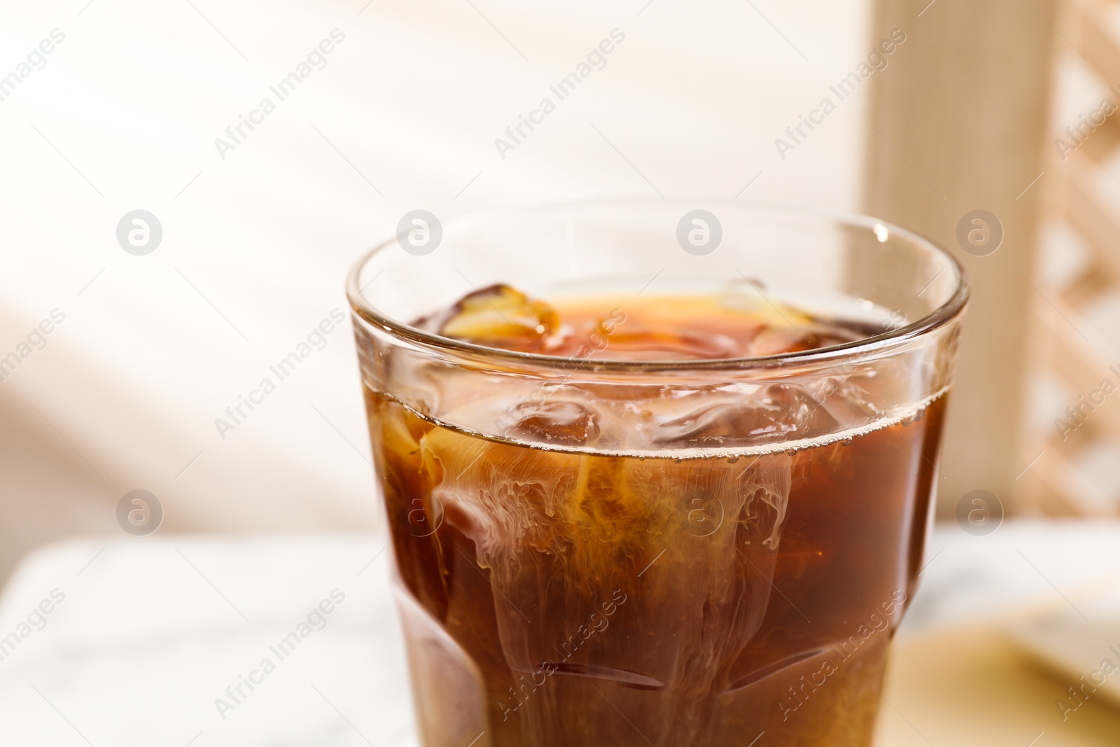 Photo of Refreshing iced coffee with milk in glass on table against blurred background, closeup