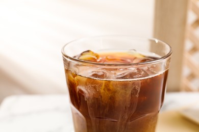 Photo of Refreshing iced coffee with milk in glass on table against blurred background, closeup