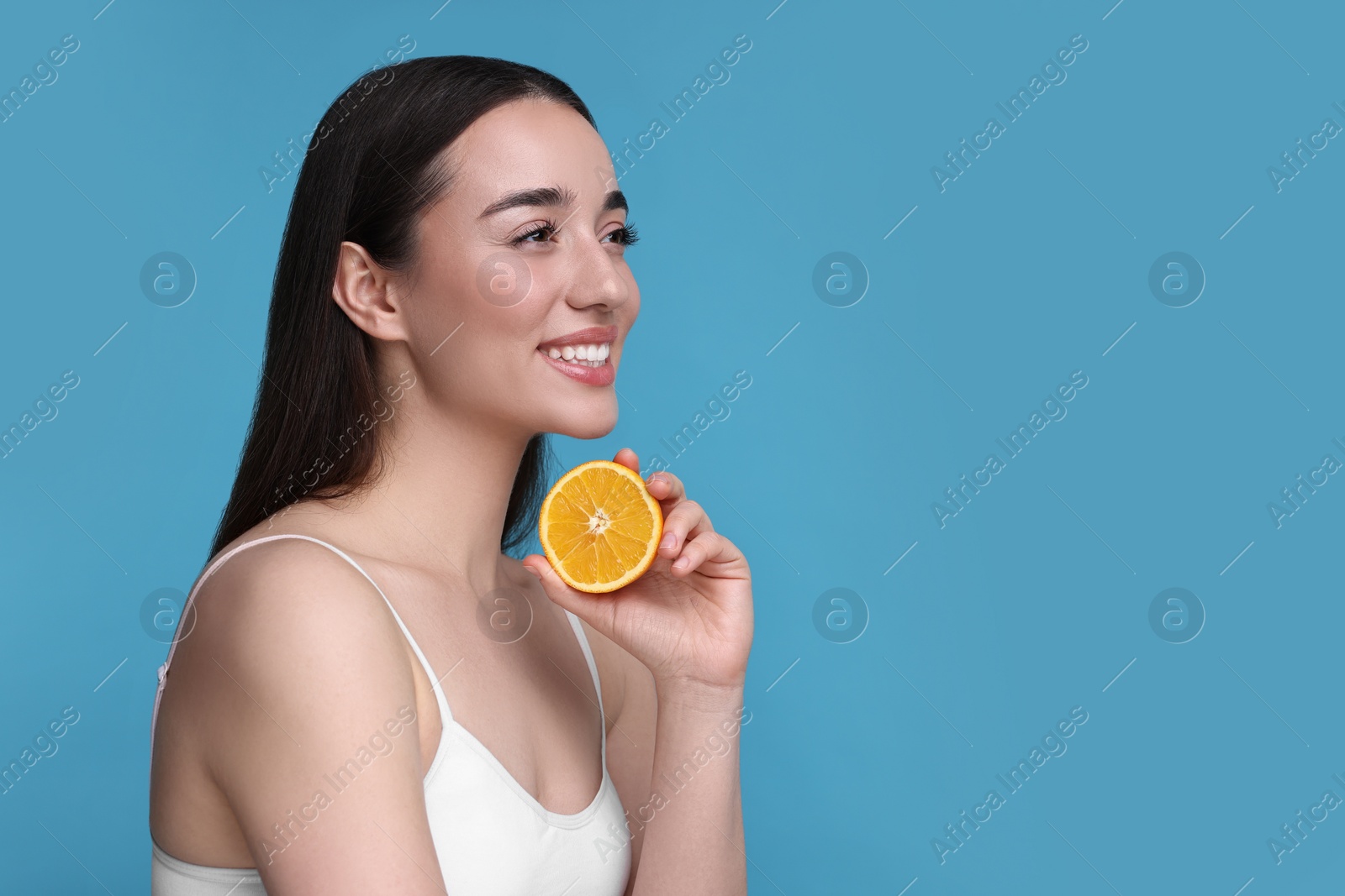 Photo of Beautiful young woman with piece of orange on light blue background. Space for text