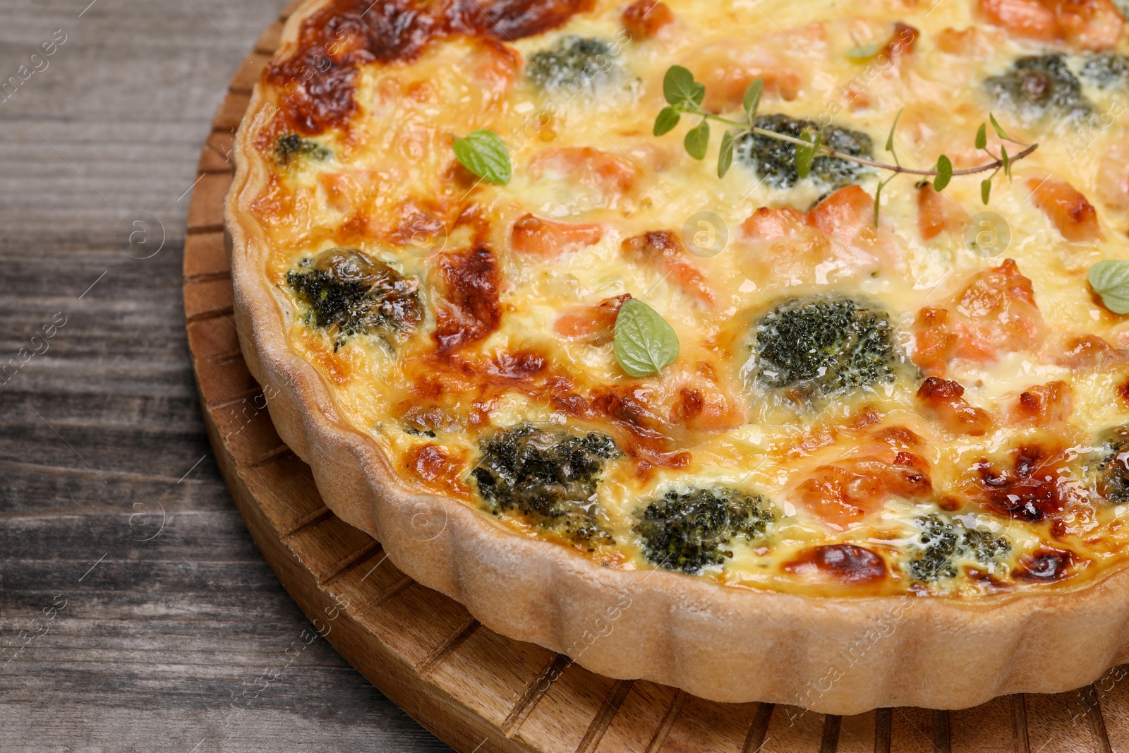 Photo of Pieces of delicious homemade quiche with salmon and broccoli on wooden board, closeup