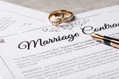 Photo of Marriage contract, fountain pen and golden wedding rings on grey table, closeup