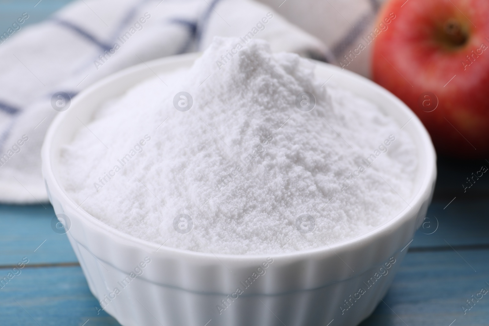 Photo of Sweet fructose powder and apple on light blue wooden table, closeup