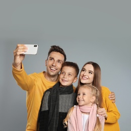 Photo of Happy family in warm clothes taking selfie on grey background. Winter season