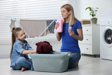 Photo of Mother smelling fabric softener while daughter taking out dirty clothes from basket in bathroom
