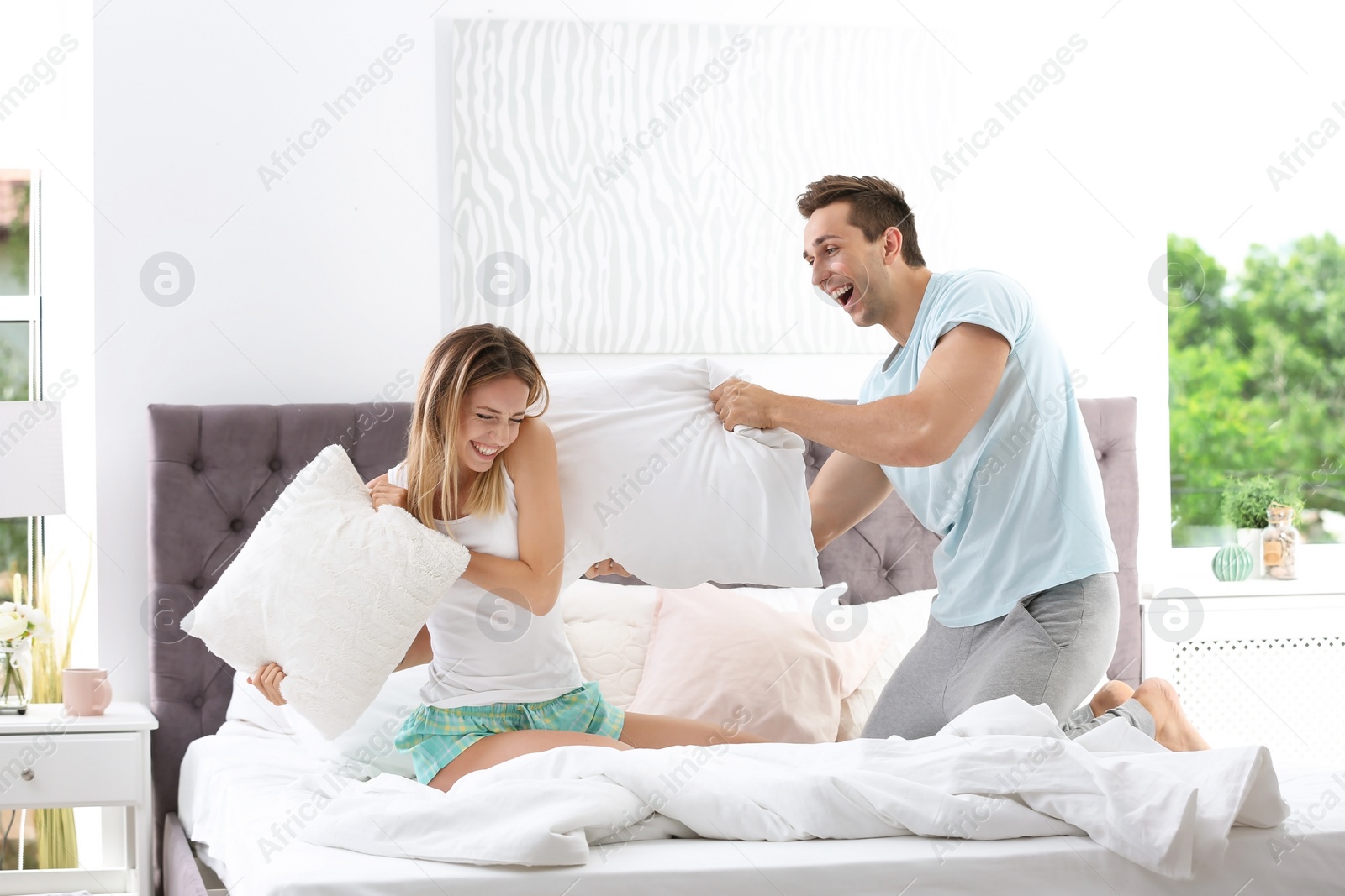 Photo of Young couple having pillow fight in bed at home