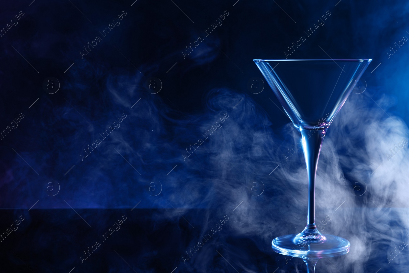 Photo of Empty clean martini glass on mirror table against black background, space for text