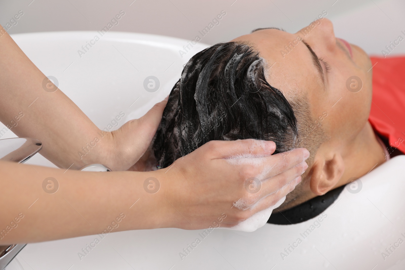 Photo of Professional hairdresser washing client's hair at sink, closeup