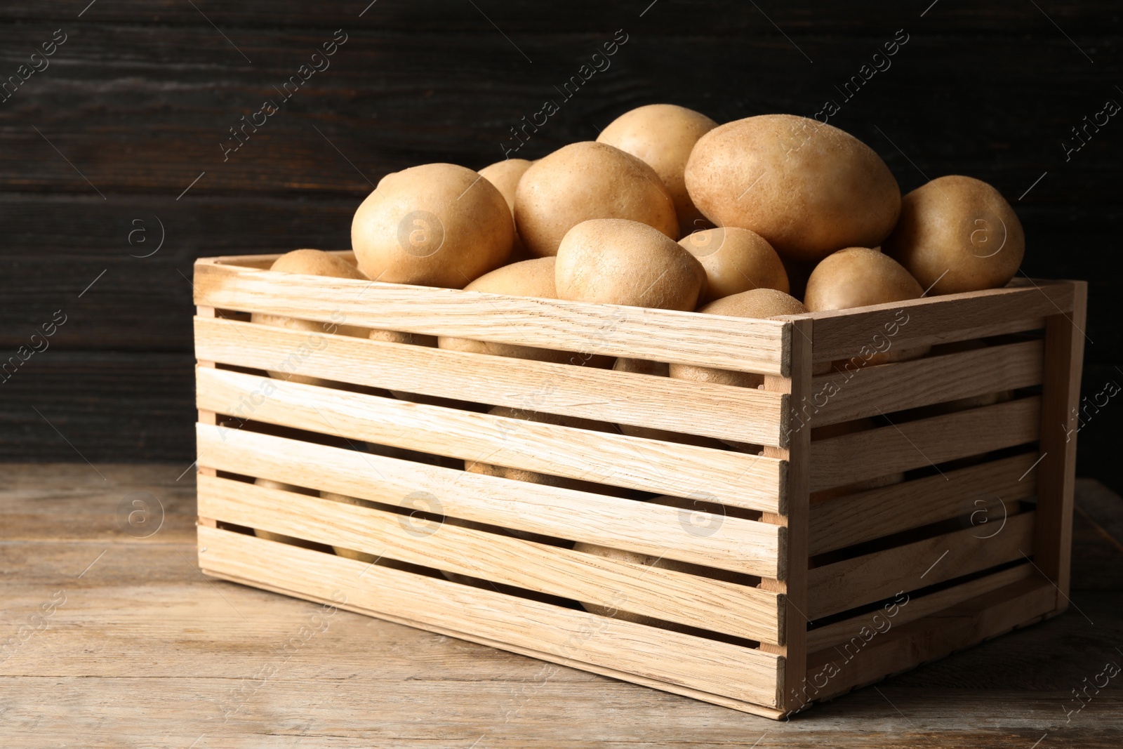 Photo of Raw fresh organic potatoes on wooden table against dark background