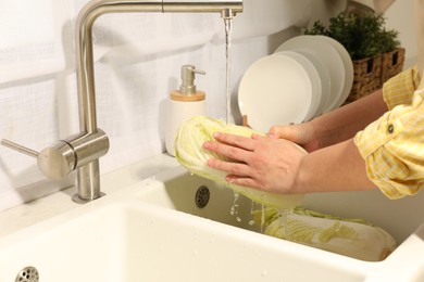 Photo of Woman washing fresh chinese cabbage under tap water in kitchen sink, closeup