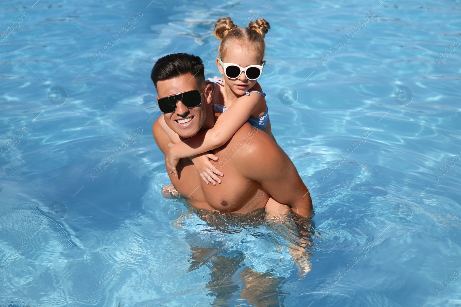 Photo of Happy man and his daughter in outdoor swimming pool on sunny summer day