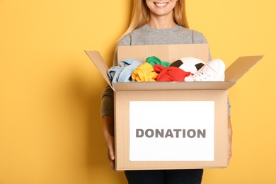 Woman holding box with donations on color background. Space for text