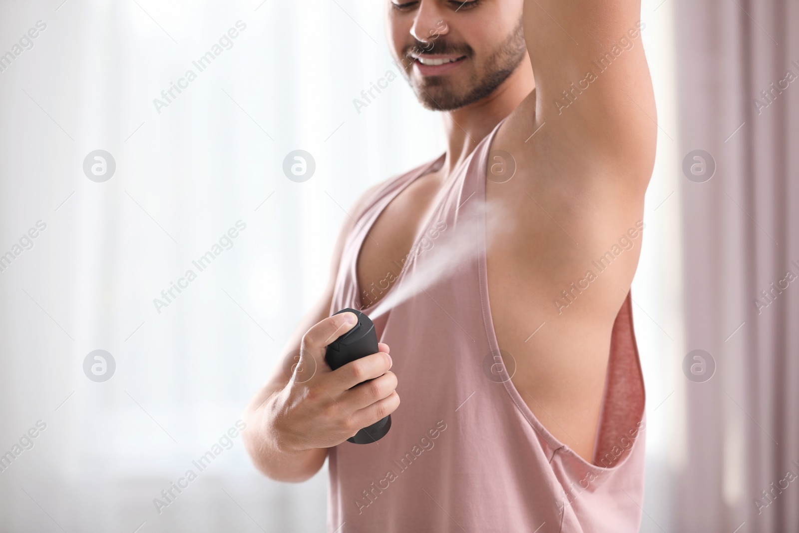 Photo of Handsome young man applying deodorant indoors. Space for text