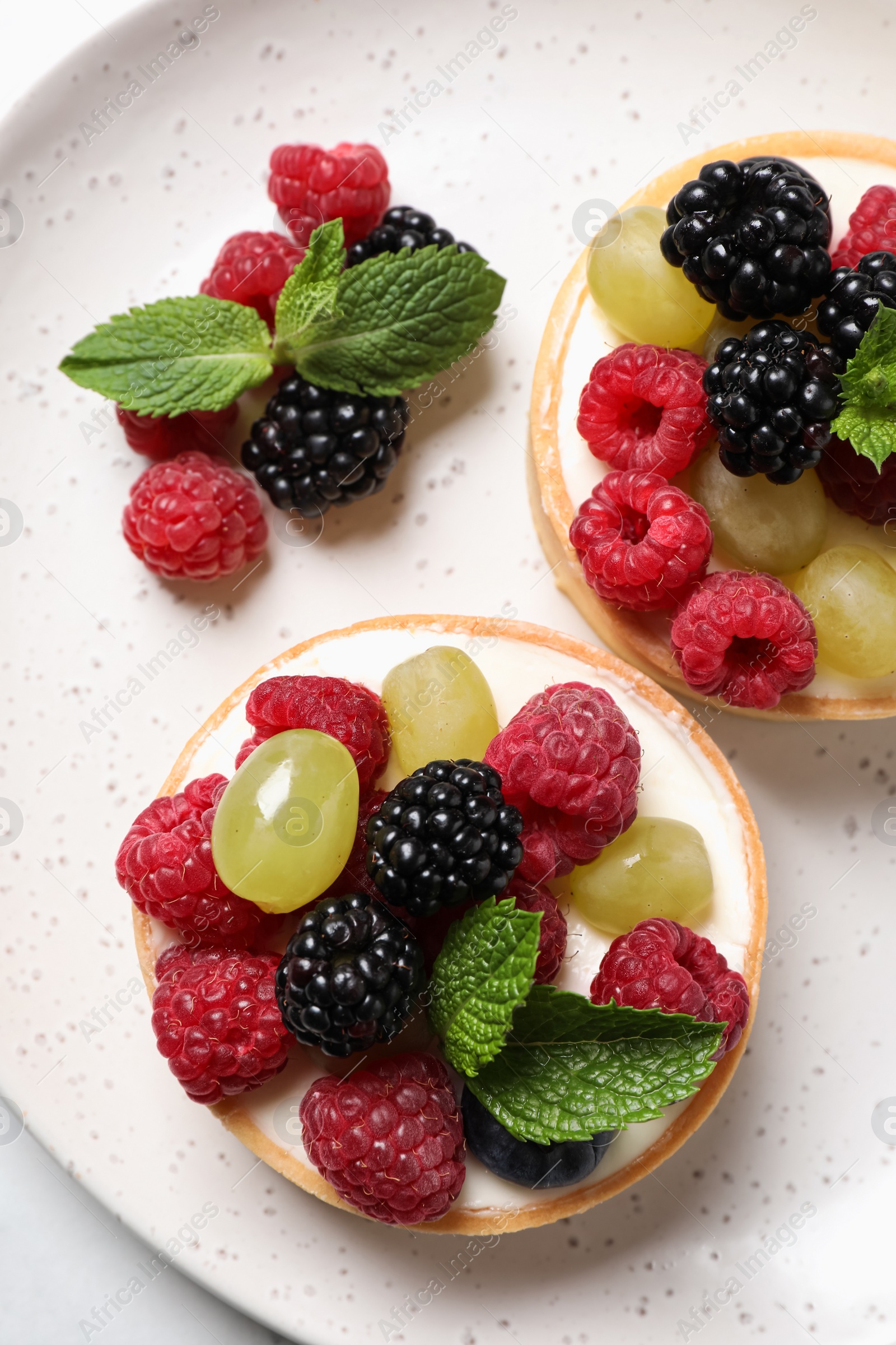 Photo of Delicious tartlets with berries on plate, top view