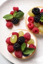 Delicious tartlets with berries on plate, top view