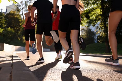Group of people running outdoors on sunny day, back view