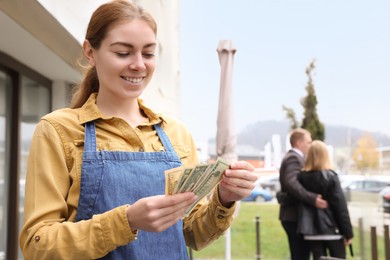 Photo of Happy waitress holding tips in outdoor cafe. Space for text