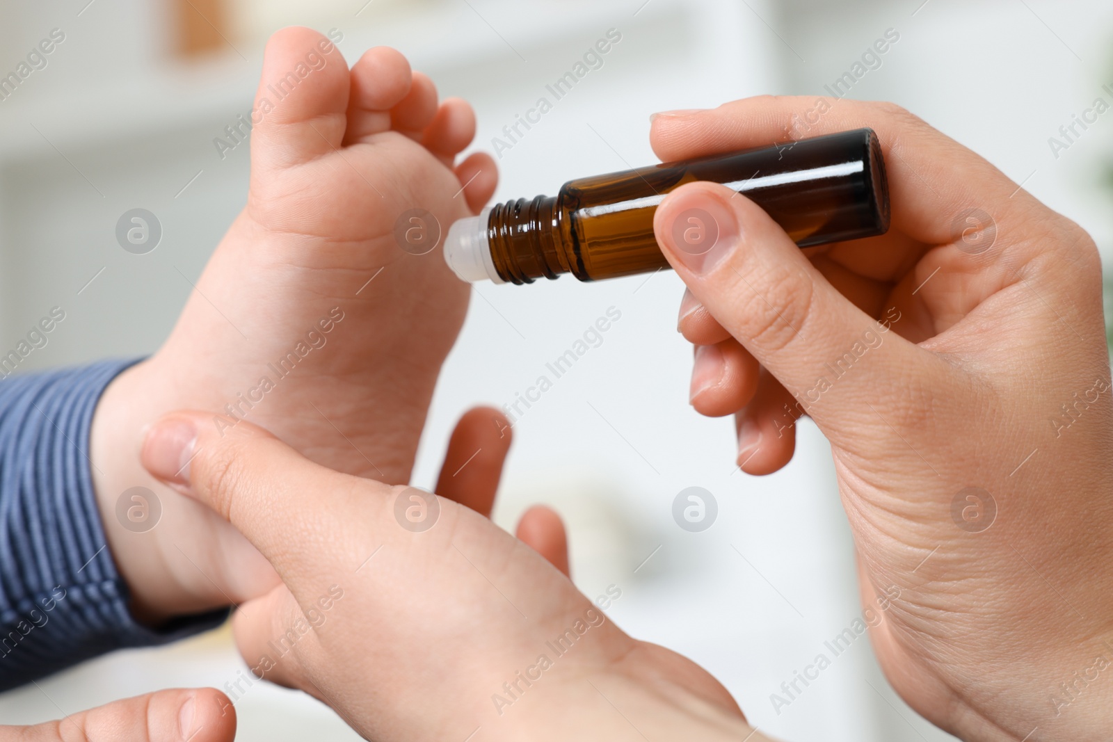 Photo of Mother applying essential oil from roller bottle onto her baby`s heel on blurred background, closeup