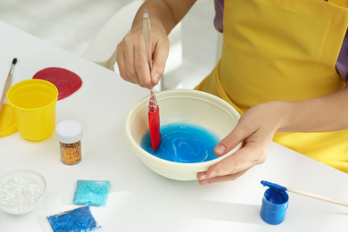 Photo of Little girl mixing ingredients with silicone spatula at table, closeup. DIY slime toy