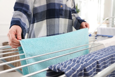 Young woman hanging clean laundry on drying rack at home, closeup