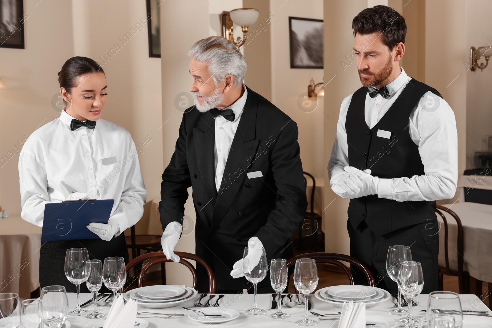 Photo of Senior man wearing formal suit teaching trainees in restaurant. Professional butler courses