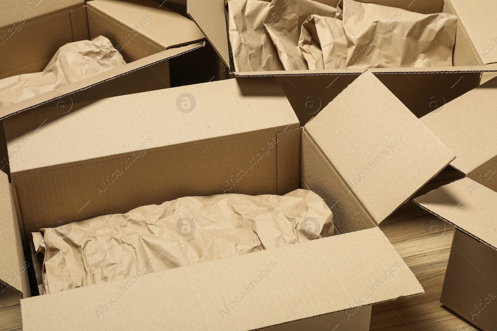 Photo of Many open cardboard boxes with crumpled paper on wooden floor