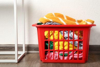Photo of Laundry basket with dirty clothes on floor near white wall