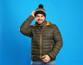 Photo of Happy young man in warm clothes on blue background. Winter vacation