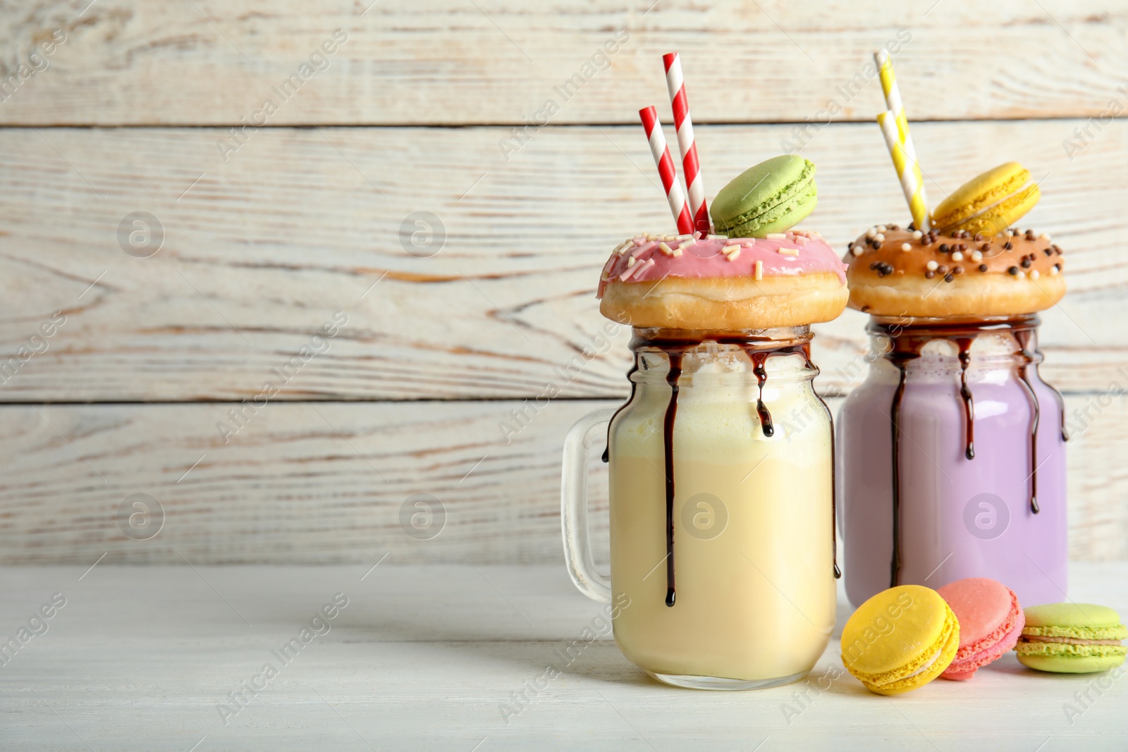 Photo of Mason jars with delicious milk shakes and macaroons on table. Space for text