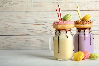 Mason jars with delicious milk shakes and macaroons on table. Space for text