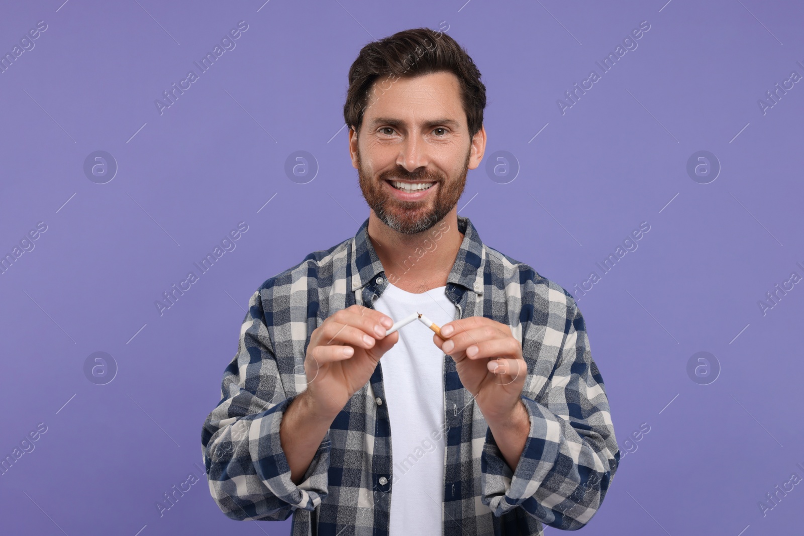 Photo of Stop smoking concept. Happy man breaking cigarette on purple background